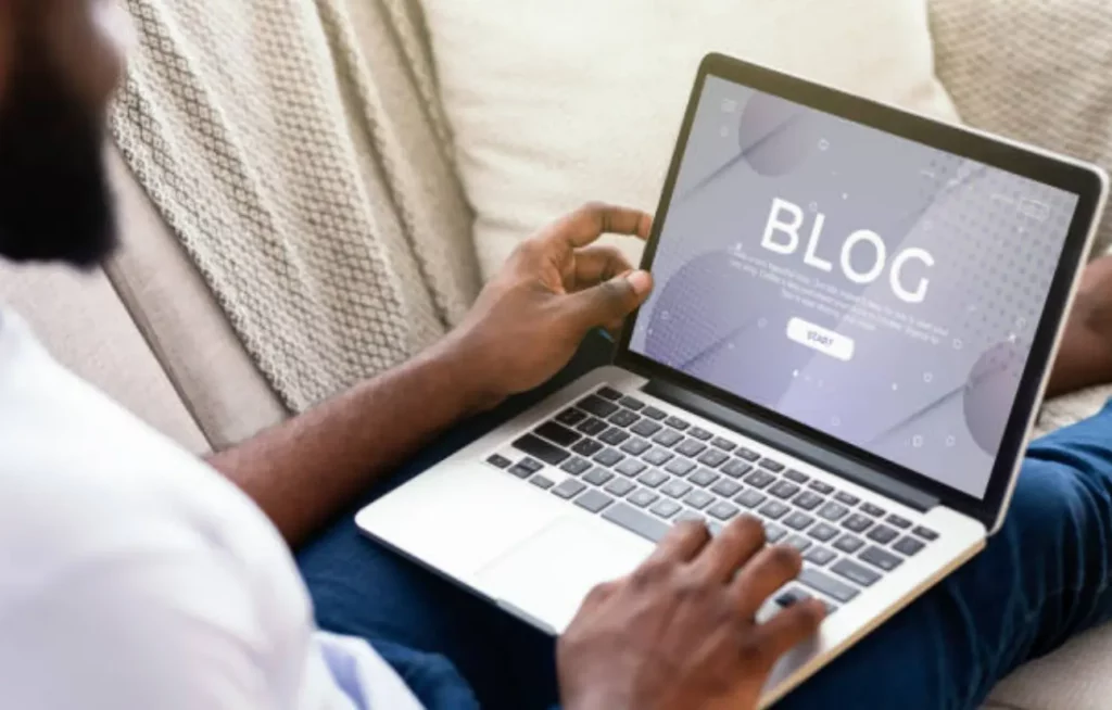 Vue par-dessus l'épaule d'une personne naviguant sur un ordinateur portable affichant le mot "BLOG" sur son écran.